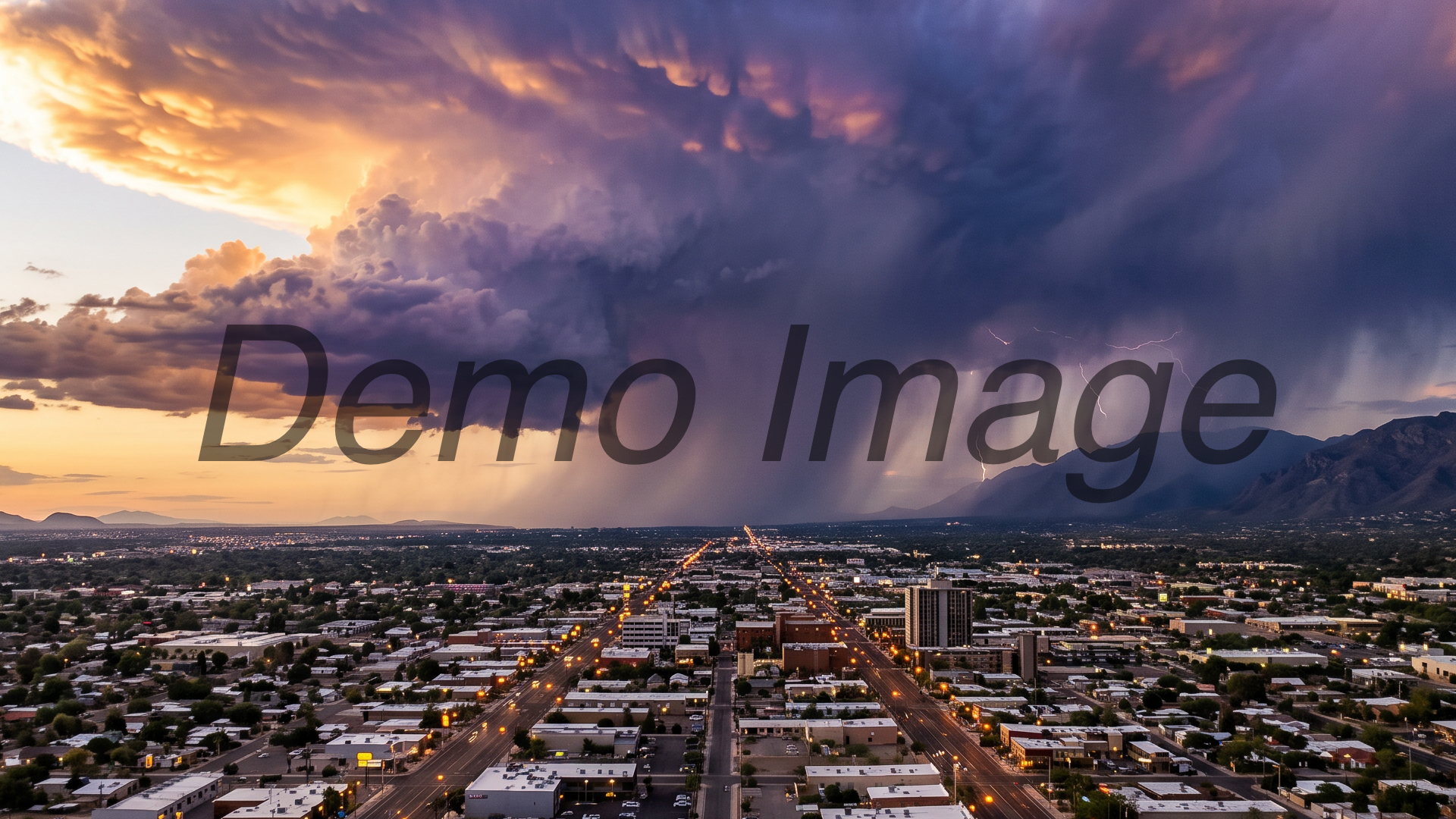 A monsoon storm cell towering over the midtown Tucson grid in late afternoon — bruised violet-and-gold anvil cloud, rain shafts over the east side, streetlights just coming on below; dramatic documentary landscape